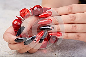 Hands with long artificial manicured nails colored with red and black nail polish