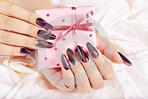 Hands with long artificial manicured nails holding a gift box