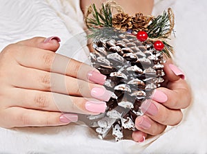 Hands with long artificial pink manicured nails holding a pine Christmas decoration