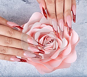 Hands with long red artificial french manicured nails and pink rose flower