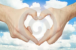 Hands make heart shape against blue sky background