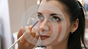 Hands make-up artist applied makeup on the face of a young woman. Girl doing eye makeup in a professional salon. Evening