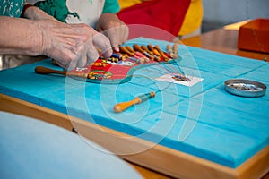 Hands making bobbin lace. Adult helps child learn craft. Colorful lace threads