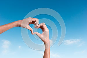 Hands making a heart shape in the blue sky