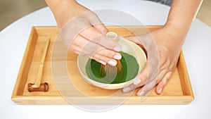 Hands making Japanese organic matcha green tea ceremony by bamboo whisk chasen on wood tray