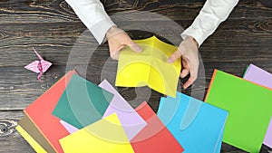 Hands making origami flower with yellow paper.