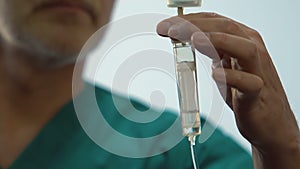 Hands of male anesthesiologist correcting dropper with painkiller for patient