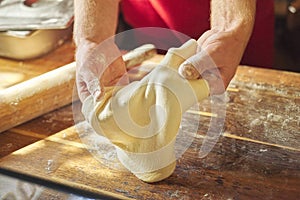 Hands of male baker with flour dough preparing food on wooden table