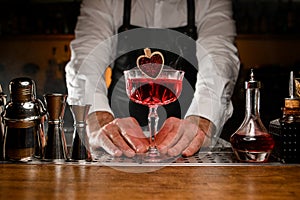 Hands of male bartender holding glass with red alcohol cocktail