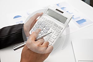 The hands of a male businesswoman use the calculator are analyzing and calculating the annual income and expenses in a financial