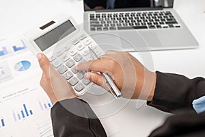 The hands of a male businesswoman use the calculator are analyzing and calculating the annual income and expenses in a financial