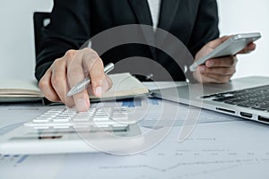 The hands of a male businesswoman use the calculator are analyzing and calculating the annual income and expenses in a financial