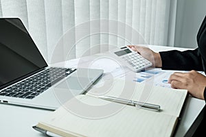 The hands of a male businesswoman use the calculator are analyzing and calculating the annual income and expenses in a financial