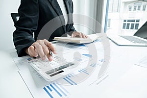 The hands of a male businesswoman use the calculator are analyzing and calculating the annual income and expenses in a financial