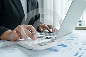 The hands of a male businesswoman use the calculator are analyzing and calculating the annual income and expenses in a financial