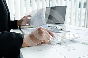 The hands of a male businesswoman use the calculator are analyzing and calculating the annual income and expenses in a financial