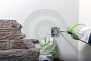 Hands of male electrician holding screwdriver working on electrical plug in residential power grid installing white ac socket on