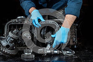 Hands of a male repairman in blue gloves on a background of a gearbox, close-up. Repair box predach, repair of used cars. Metal