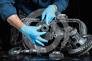 Hands of a male repairman in blue gloves on a background of a gearbox, close-up. Repair box predach, repair of used cars. Metal