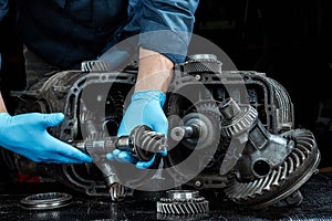 Hands of a male repairman in blue gloves on a background of a gearbox, close-up. Repair box predach, repair of used cars. Metal