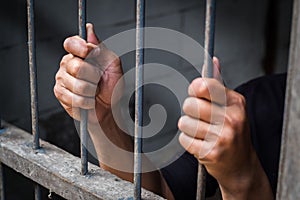 Hands of man behind jail bars.