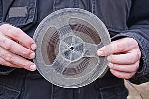 hands of a man in black clothes holding one old plastic brown gray magnetic reel