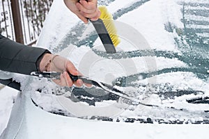 Hands of a man with a brush cleaning the windshield of a car from snow in the winter season