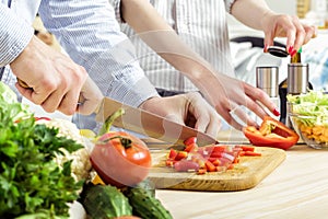 Hands of man chopped red bell pepper on board. Couple chopping vegetables in kitchen