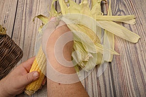 Hands of a man cleaning an ear of corn on a wooden background. Autumn harvest, Healthy food, Fitness diet. Close up