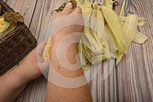 Hands of a man cleaning an ear of corn on a wooden background. Autumn harvest, Healthy food, Fitness diet. Close up