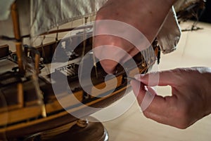 A hands of a man delicately working a model of a miniature ship piece by piece