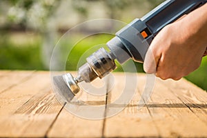 Hands man with electrical rotating brush metal disk sanding a piece of wood