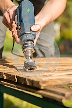 Hands man with electrical rotating brush metal disk sanding a piece of wood