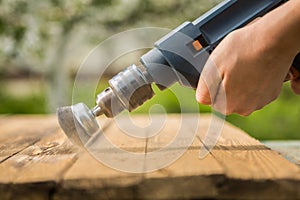 Hands man with electrical rotating brush metal disk sanding a piece of wood