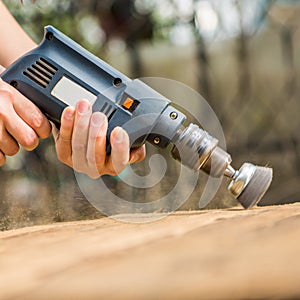 Hands man with electrical rotating brush metal disk sanding a piece of wood