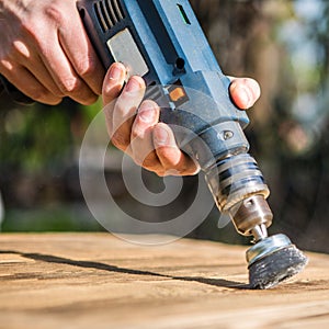 Hands man with electrical rotating brush metal disk sanding a piece of wood