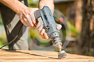 Hands man with electrical rotating brush metal disk sanding a piece of wood