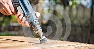 Hands man with electrical rotating brush metal disk sanding a piece of wood