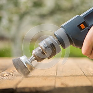 Hands man with electrical rotating brush metal disk sanding a piece of wood