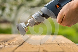 Hands man with electrical rotating brush metal disk sanding a piece of wood