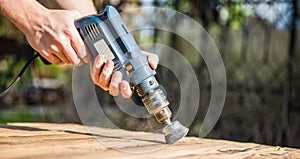 Hands man with electrical rotating brush metal disk sanding a piece of wood