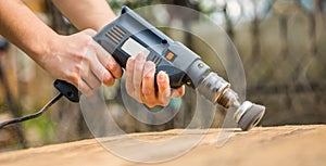 Hands man with electrical rotating brush metal disk sanding a piece of wood