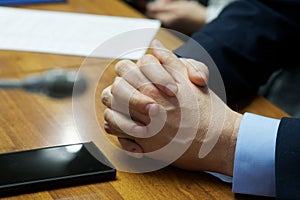 Hands of a man in an elegant suit, a businessman or an official sitting at a desk, next to a smartphone. Waiting for a call or