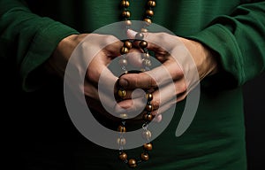 Hands of a man in a green cassock holding a rosary beads