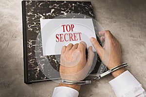 Hands of a man in handcuffs on a folder with top secret information, the concept of punishment for divulging state secrets