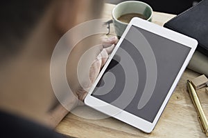 Hands of a man holding blank tablet device over a wooden workspace table