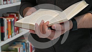 Hands of a man holding a book in a bookstore or library on a background with many different bookshelves