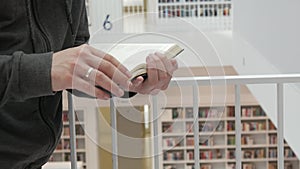 Hands of a man holding a book in a bookstore or library on a background with many different bookshelves