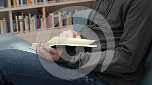 Hands of a man holding a book in a bookstore or library on a background with many different bookshelves