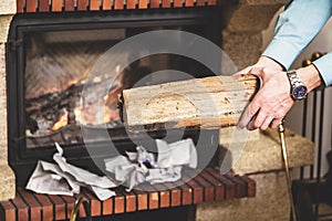 Hands of man holding piece of wood in front fireplace